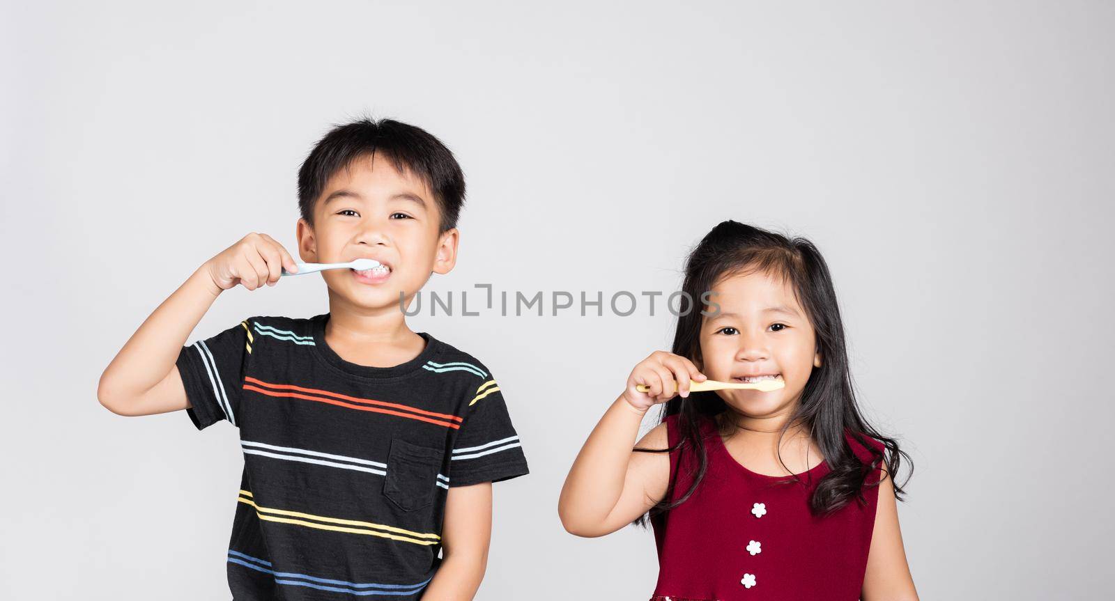 Little cute kid boy and girl 3-6 years old brushing teeth and smile in studio shot isolated on white background, happy Asian children holding toothbrush in mouth by himself, Dental hygiene healthy