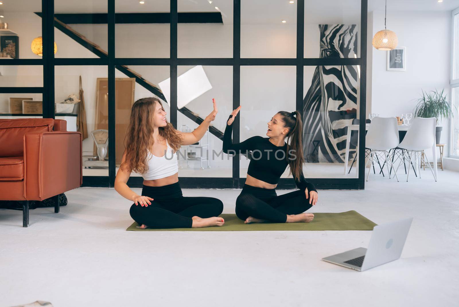 Two women while sitting in the lotus position give a high five by teksomolika