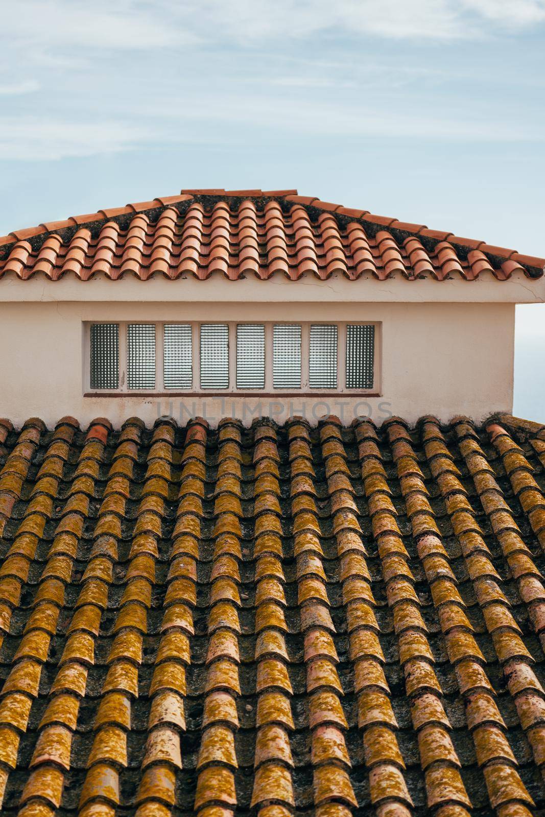 Roof of a house with small window and terracotta tiles. by apavlin