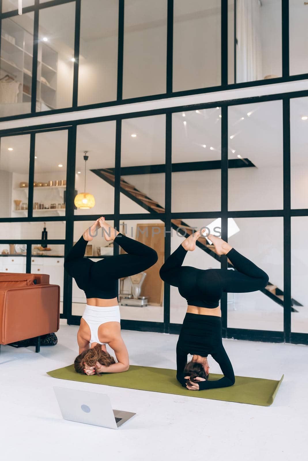 Two young woman working out indoors, doing yoga exercise on mat by teksomolika