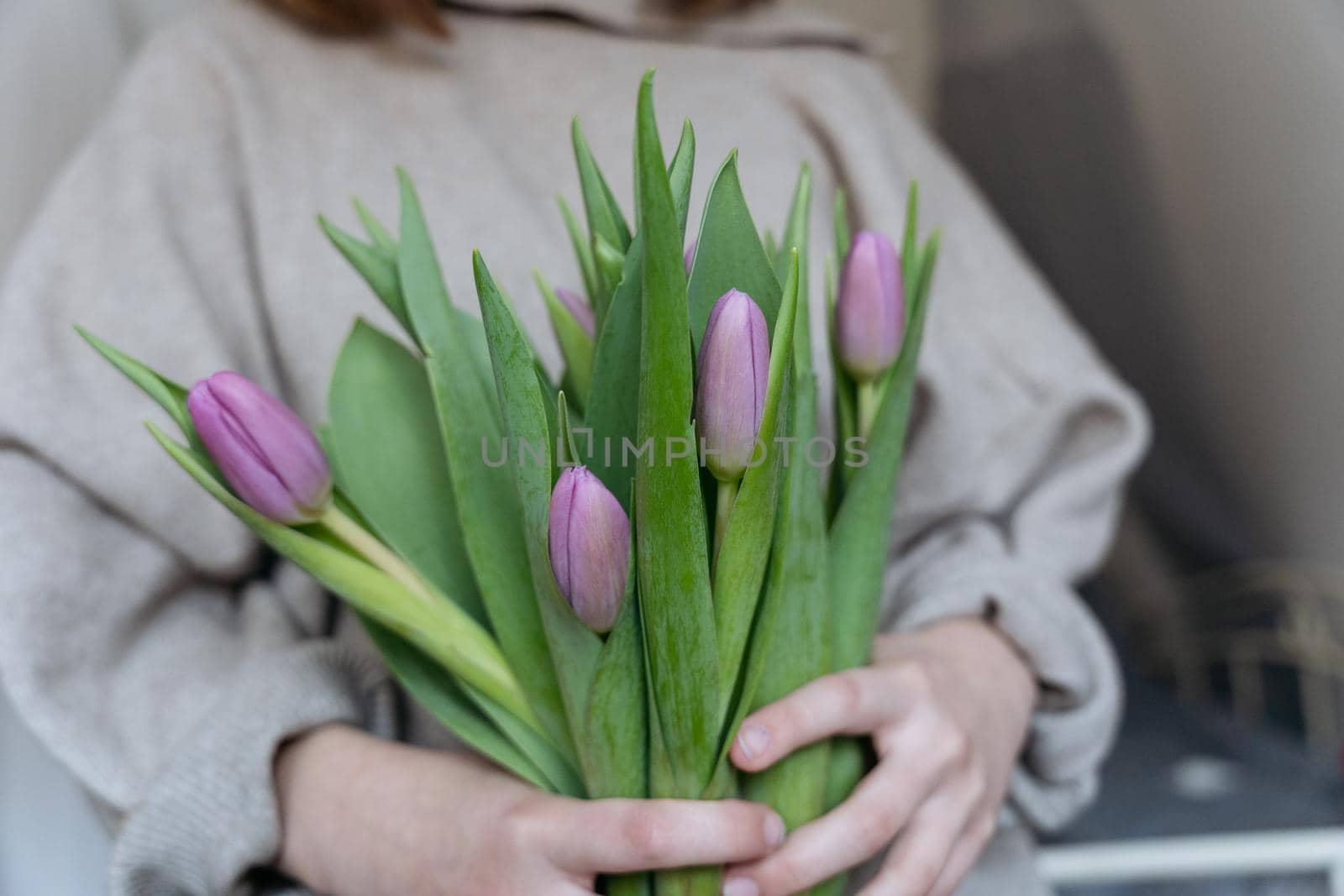 Close-up of a young woman wearing a beige jumper and holding a bunch of pink tulips