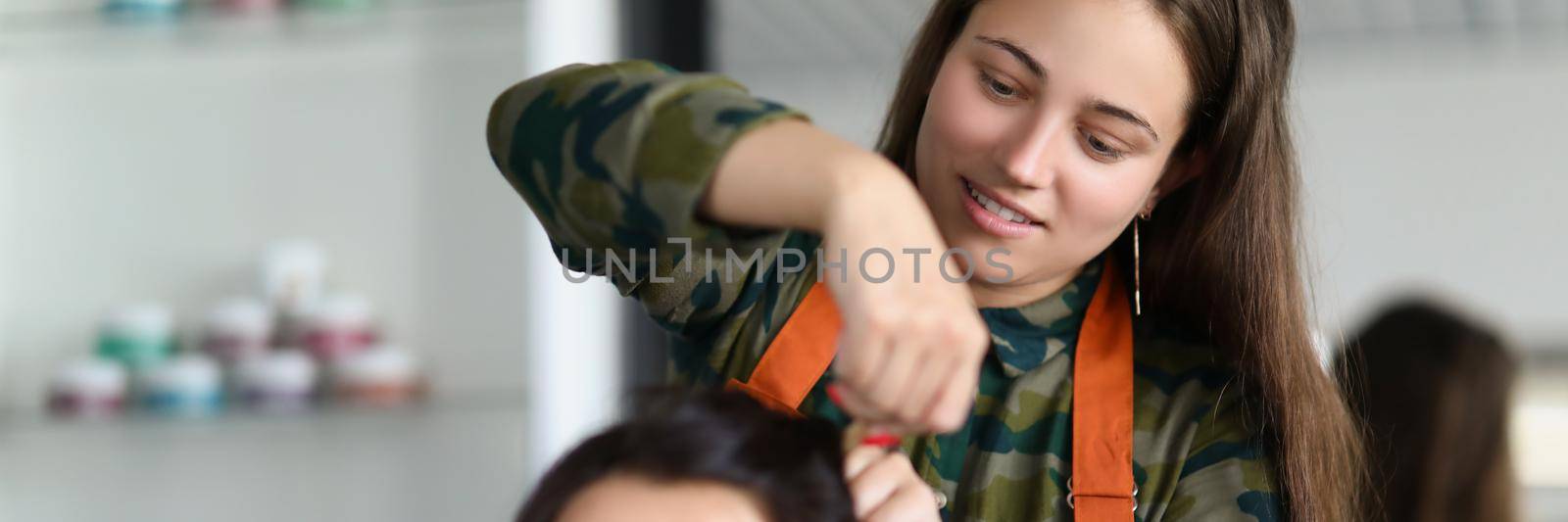 Portrait of smiling hairdresser creating fancy hairstyle for female client. Prepare woman for important event in beauty salon. Wellness, barbershop concept