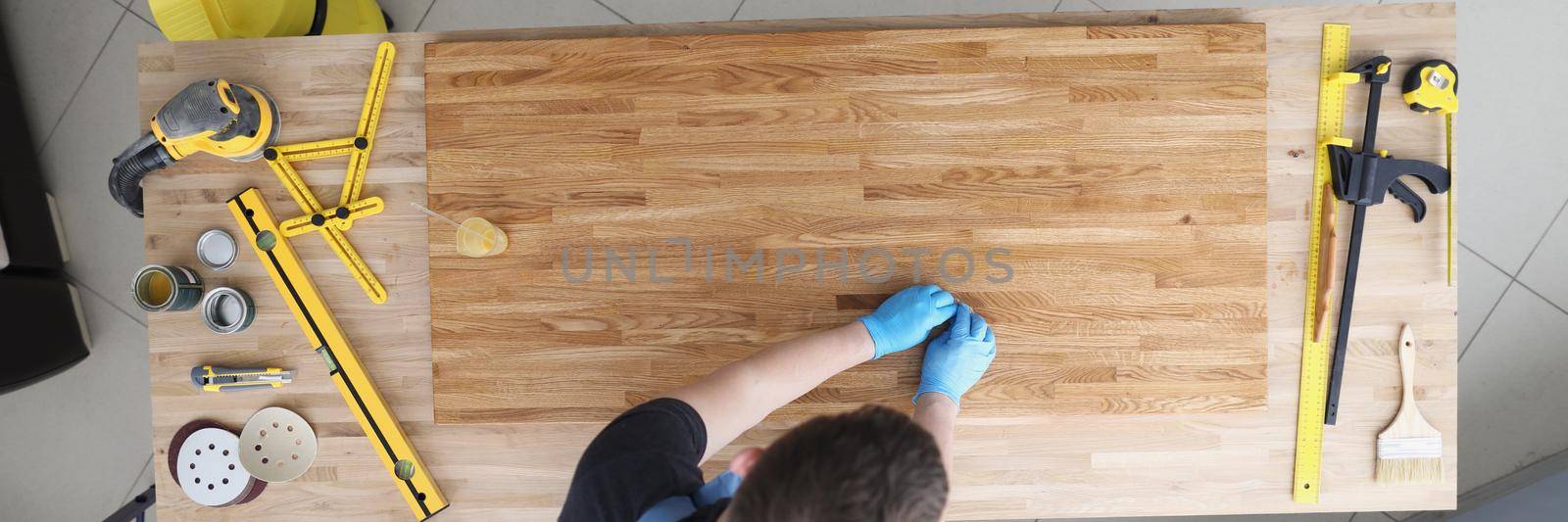 Top view of carpenter male lacquer wooden plank at work, qualified worker cover wood part of furniture with varnish. Carpentry work, renovation concept