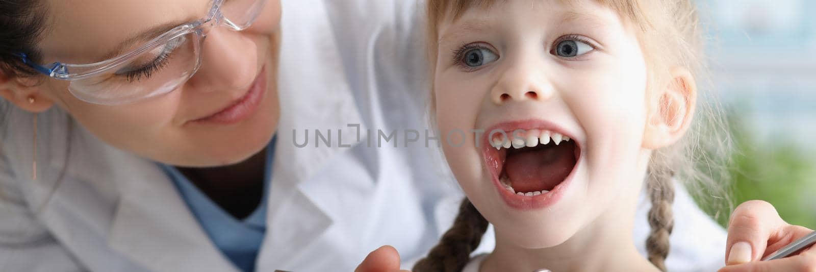 Child visiting family doctor, pediatrician with tool check throat, girl open mouth wide by kuprevich