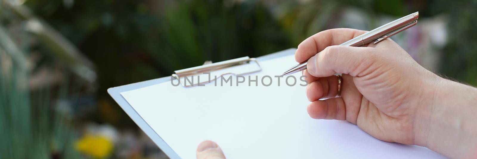 Human hand writing on clipboard with white paper, pen and blank document by kuprevich