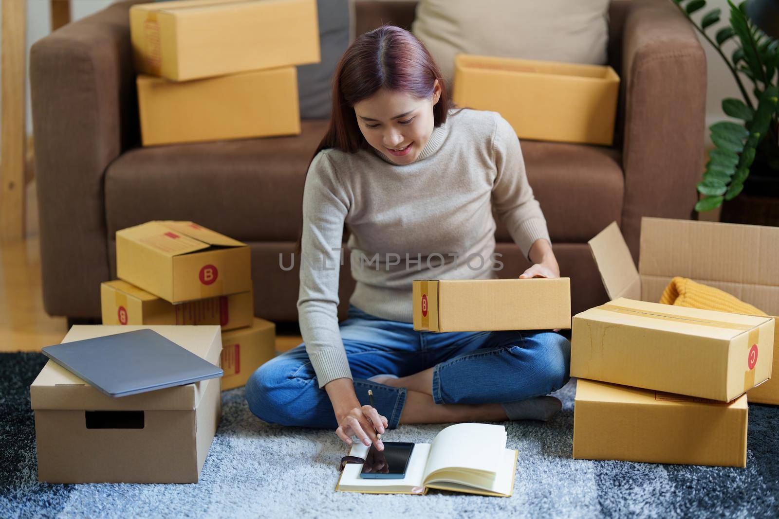 Image of Young asian woman startup freelance with parcel box and talking with customer by tablet. Online marketing packing box delivery concept. by itchaznong
