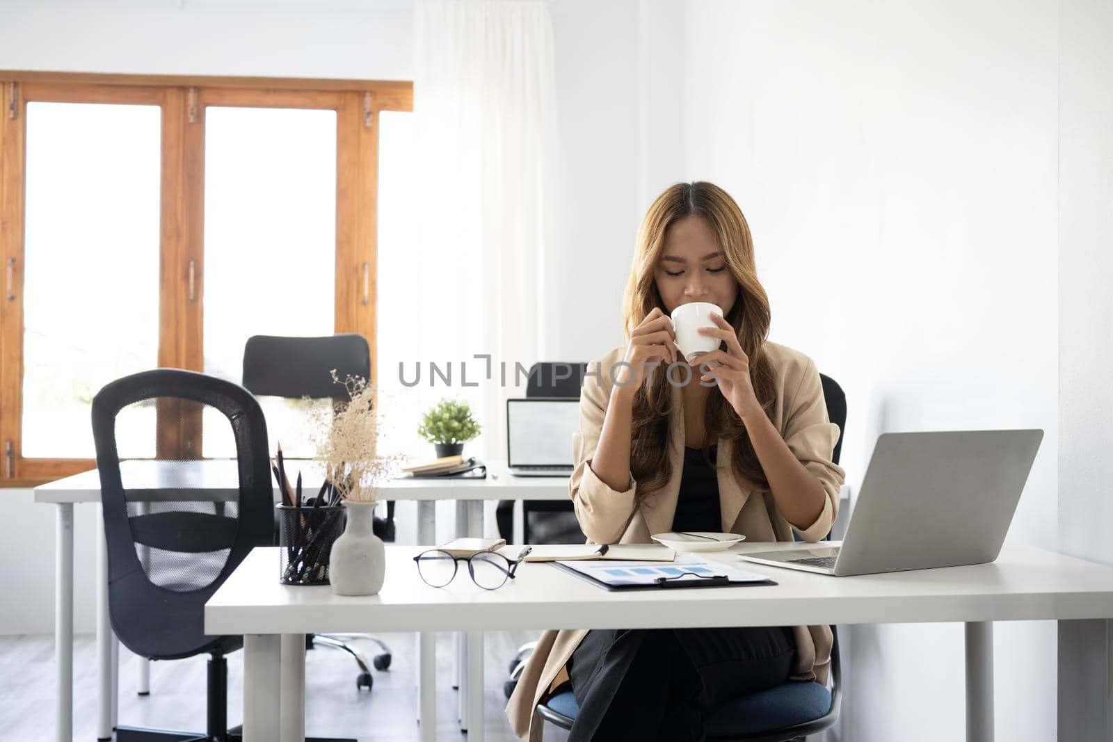 Asian businesswoman relaxing in office and drinking hot coffee.