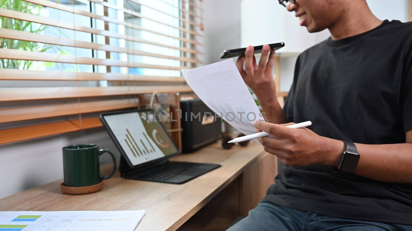 Smiling asian man freelancer talking on mobile phone and working with computer tablet.