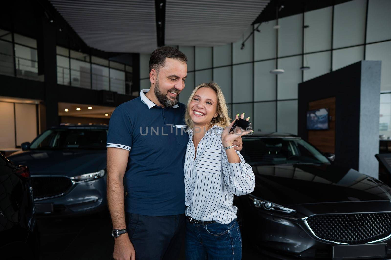 Happy caucasian couple hugging and woman holding new car keys in car showroom. by mrwed54