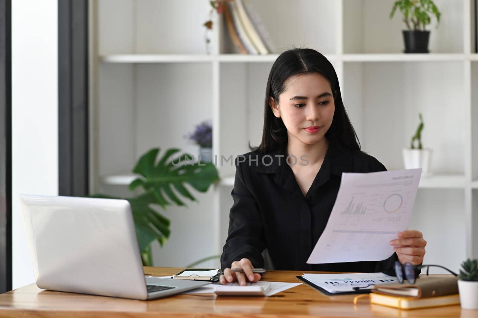 Successful businesswoman analyzing financial reports at her workplace. by prathanchorruangsak