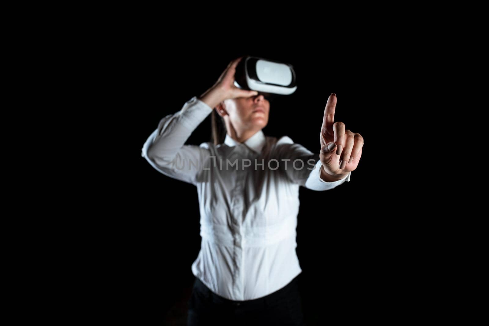 Female Professional Wearing Virtual Reality Headset Gesturing And Enjoying Simulator. Elegant Businesswoman Presenting Modern Technology And Using Futuristic Gadget. by nialowwa