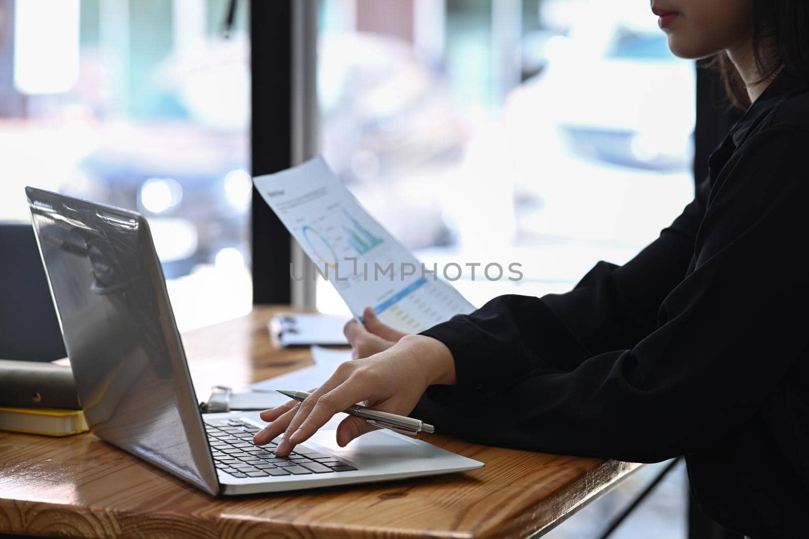 Businesswoman holding paperwork and searching information on laptop computer. by prathanchorruangsak