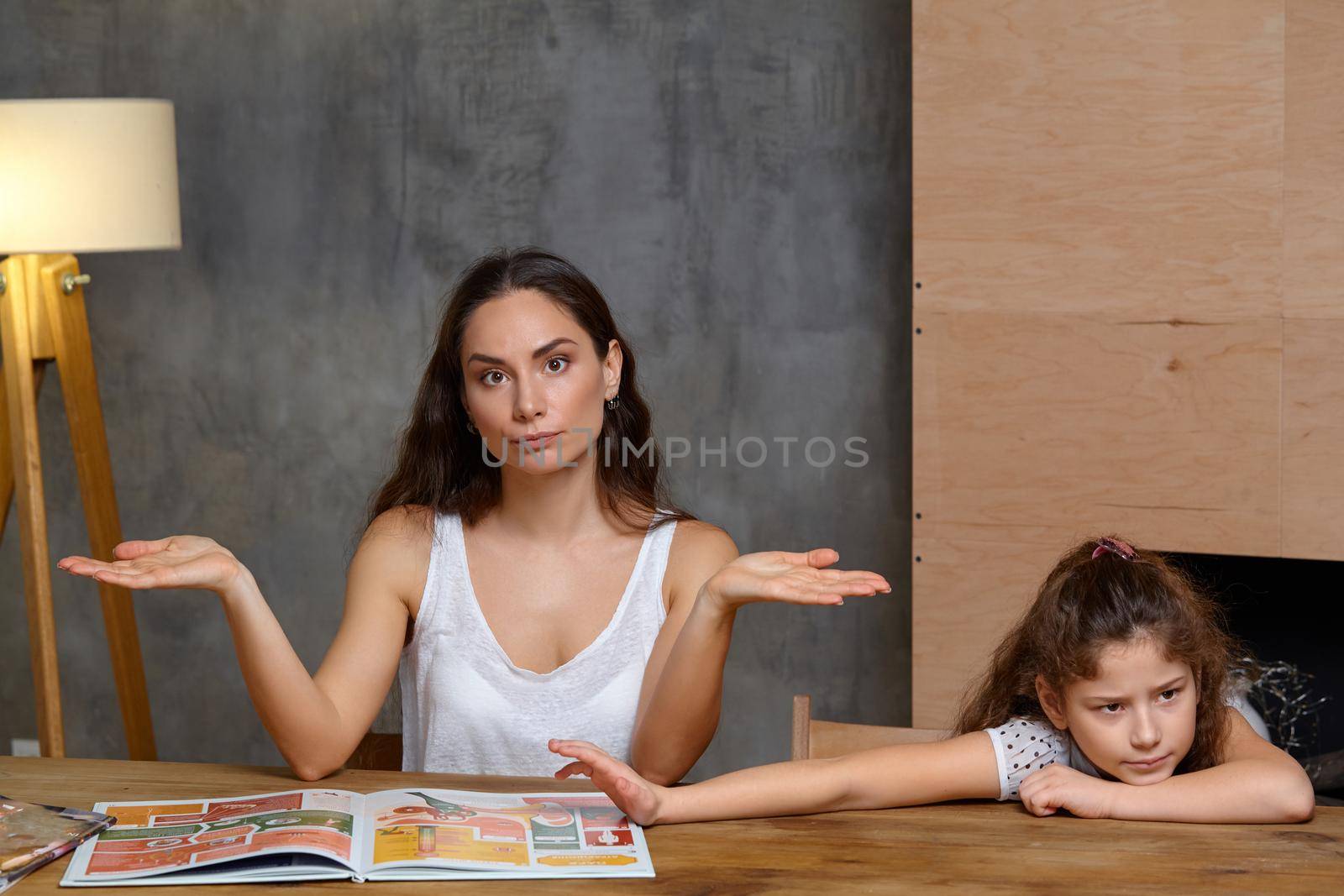 Portrait of a mother helping her small sweet and cute daughter to make her homework indoors. They both are disappointed.