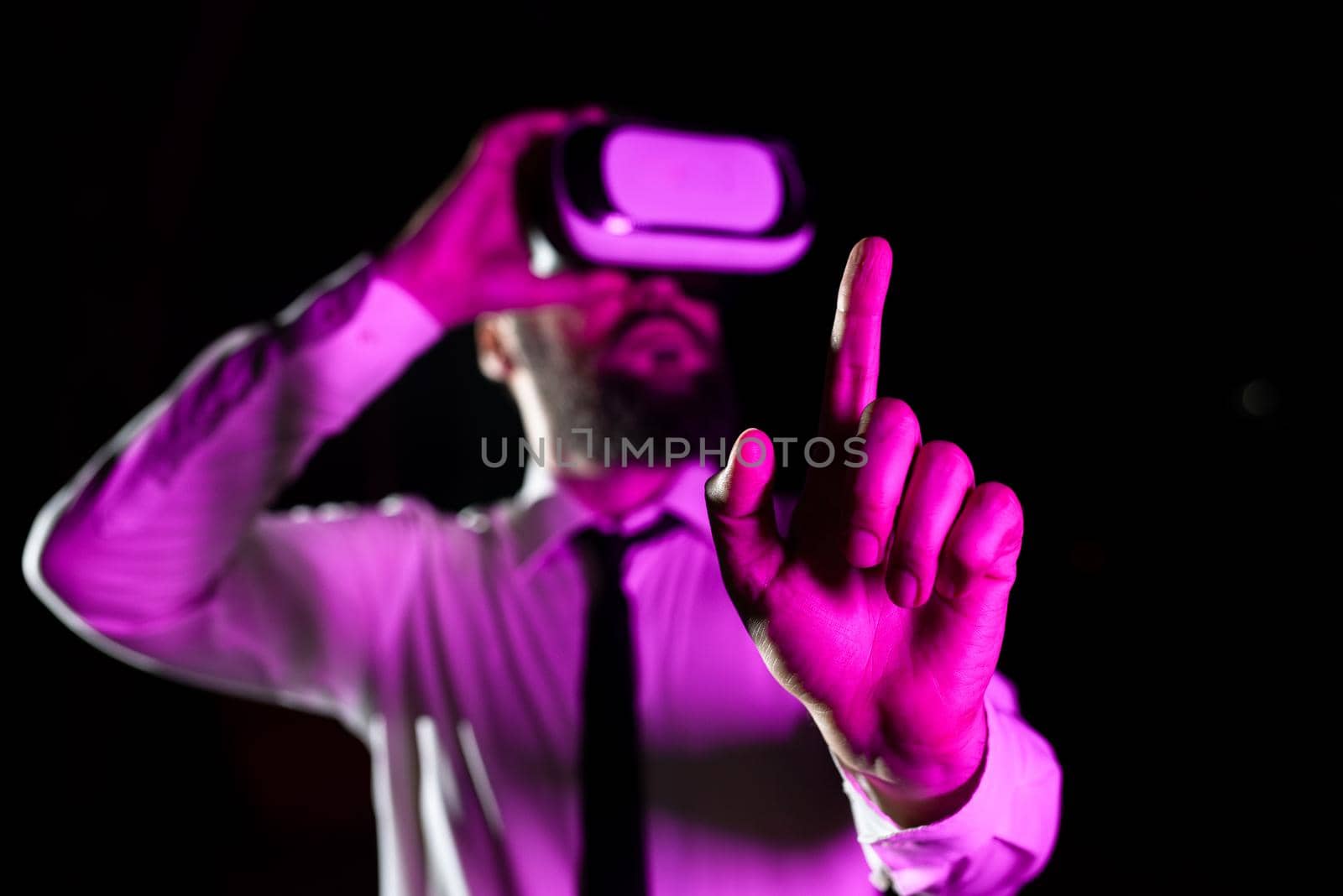 Male Professional Wearing Virtual Reality Headset Gesturing And Enjoying Simulator. Light Falling On Businessman Presenting Modern Technology And Using Modern Gadget. by nialowwa