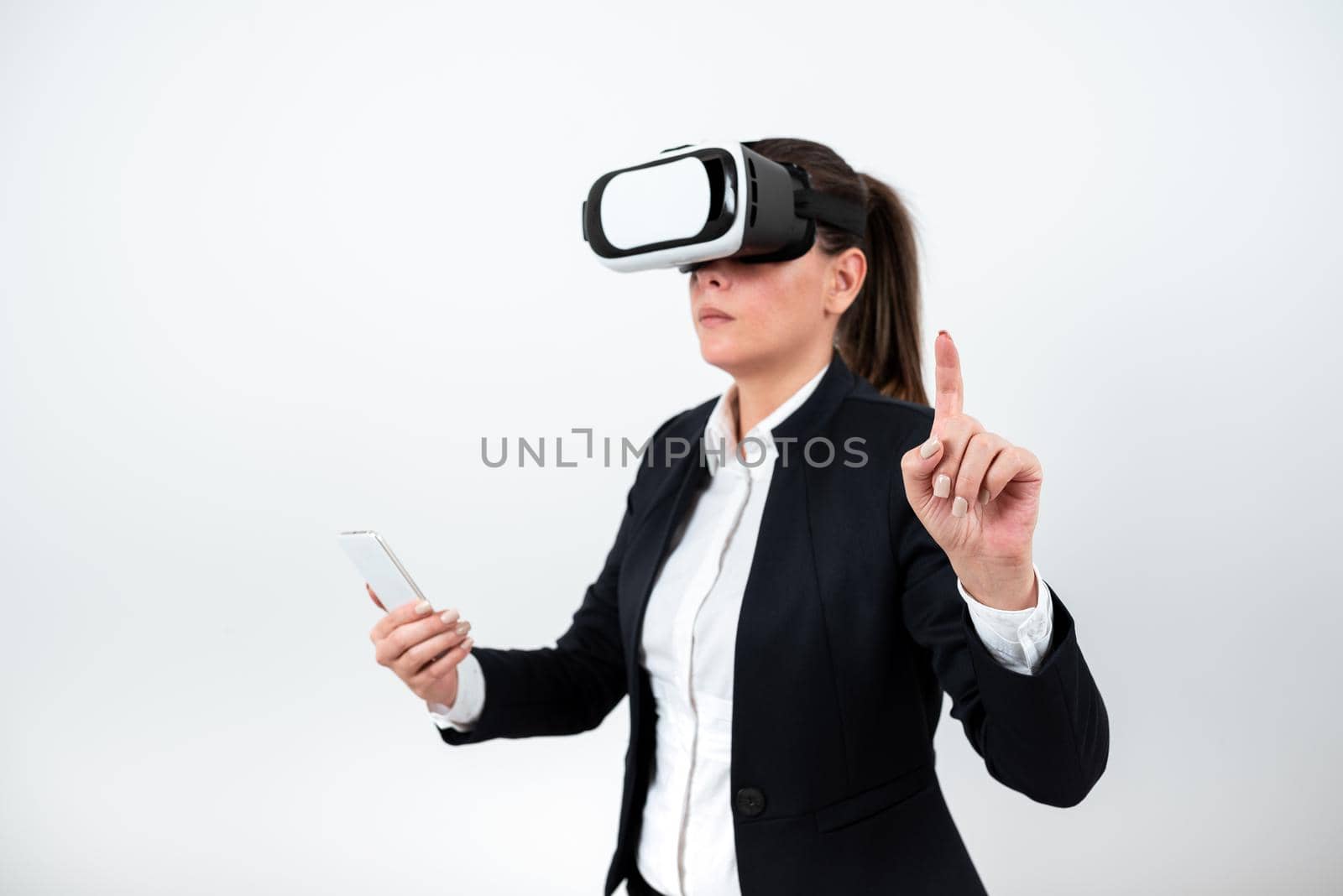 Woman Holding Mobile Phone, Wearing Vr Glasses And Pointing On Recent Update With One Finger. Businesswoman Having Virtual Reality Eyeglasses, Cellphone And Presenting New Idea by nialowwa