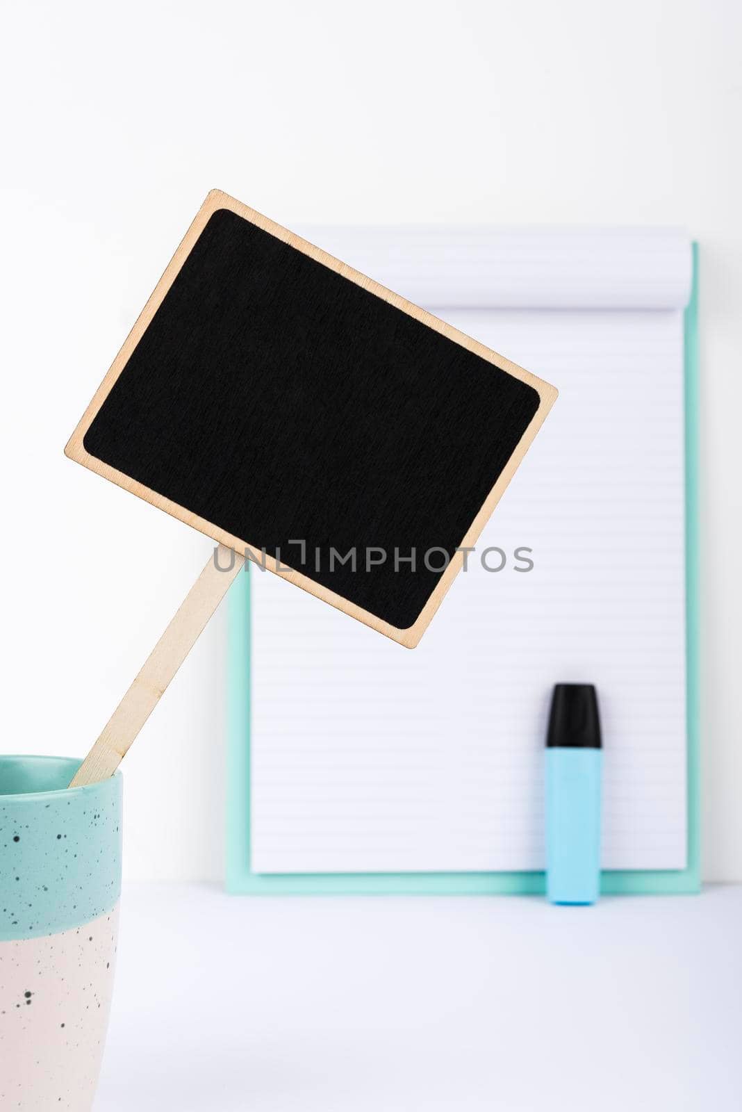 Small Blackboard With Important Message In Cup On Desk With Clipboard And Marker. Little Board With Crutial Information On Table With Paper. Current Ideas Presented. by nialowwa