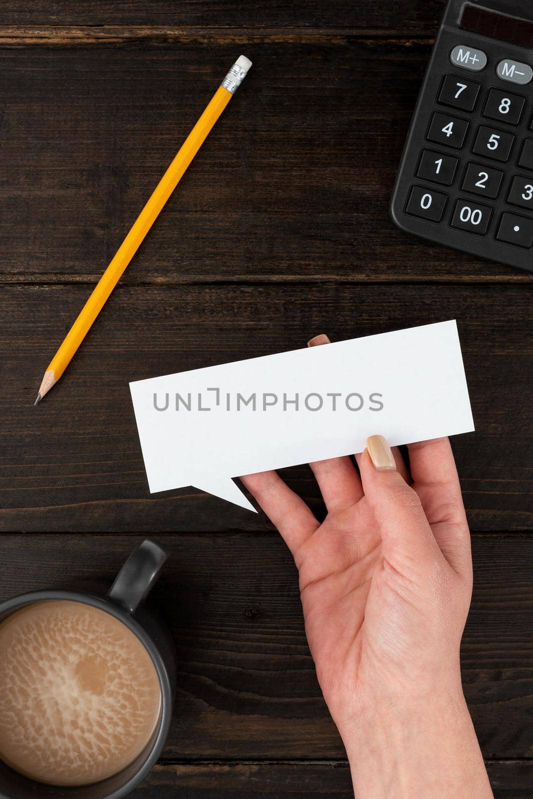 Hand Of Woman Having Thought Bubble Sheet With Coffee Cup And Stationery Over Wooden Background. Businesswoman Holding Blank Paper With Copy Space For Business Branding. by nialowwa