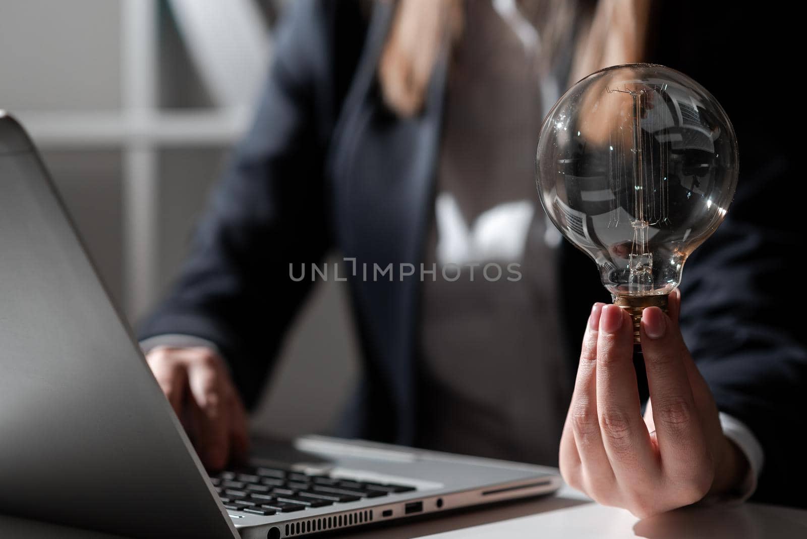 Businesswoman Typing Recent Updates On Lap Top On Desk Holding Lightbulb.