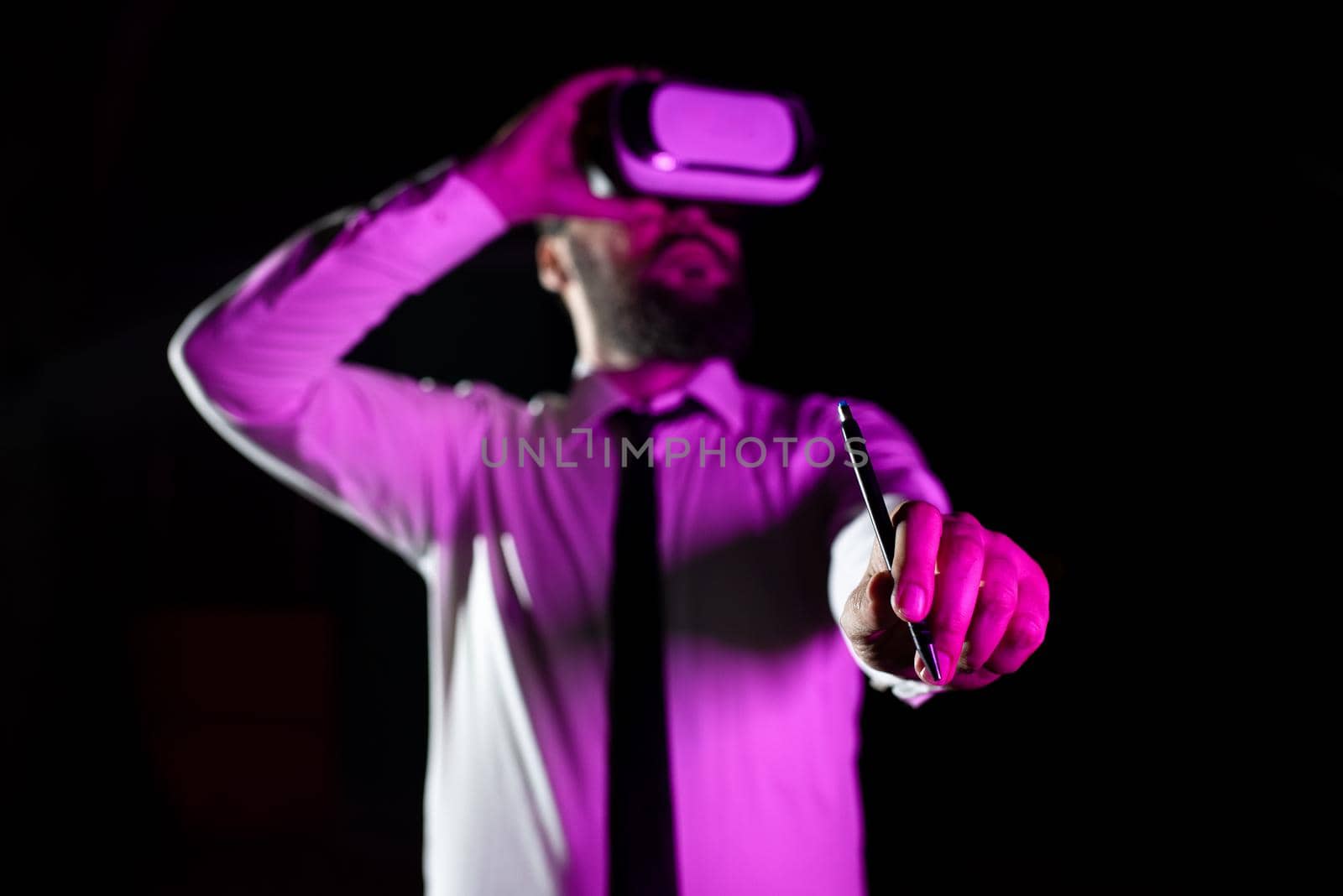 Businessman Wearing Headset Holding Pen While Taking Professional Training Through Wearing Virtual Reality Simulator. Light Falling On Man Presenting Futuristic Technology. by nialowwa