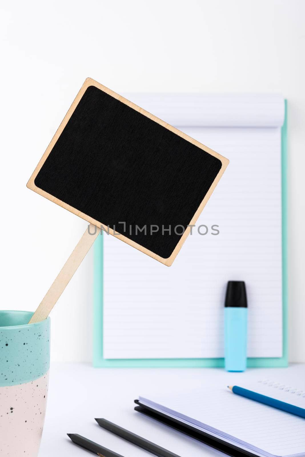 Small Blackboard With Important Message In Cup On Desk With Clipboard, Notebooks And Marker. Little Board With Crutial Information On Table With Paper. Current Ideas Presented by nialowwa