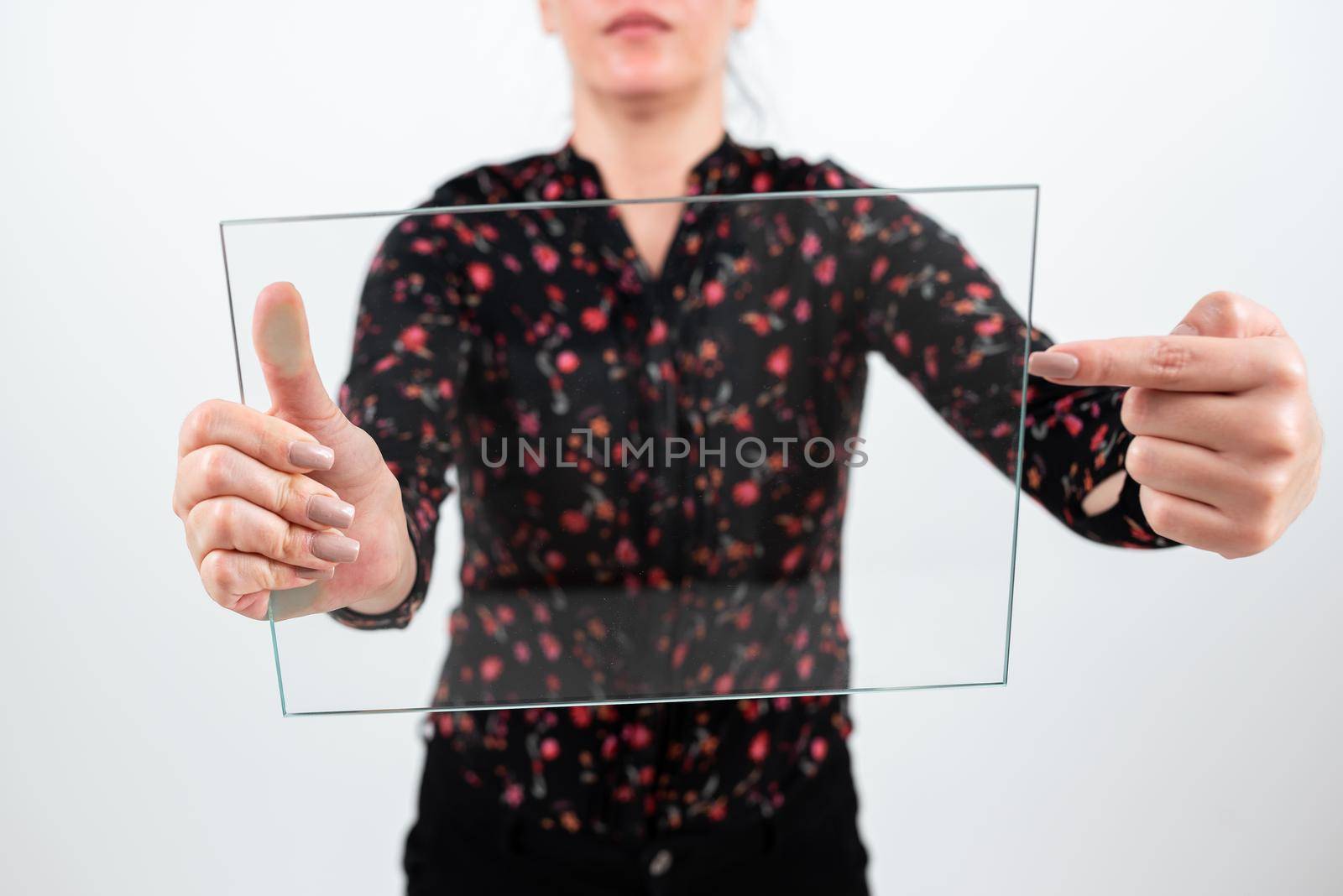 Businesswoman Holding And Pointing Transparent Glass While Presenting Important Information. Woman Wearing Floral T-Shirt Showing Rectangular Banner For Brand Promotion. by nialowwa