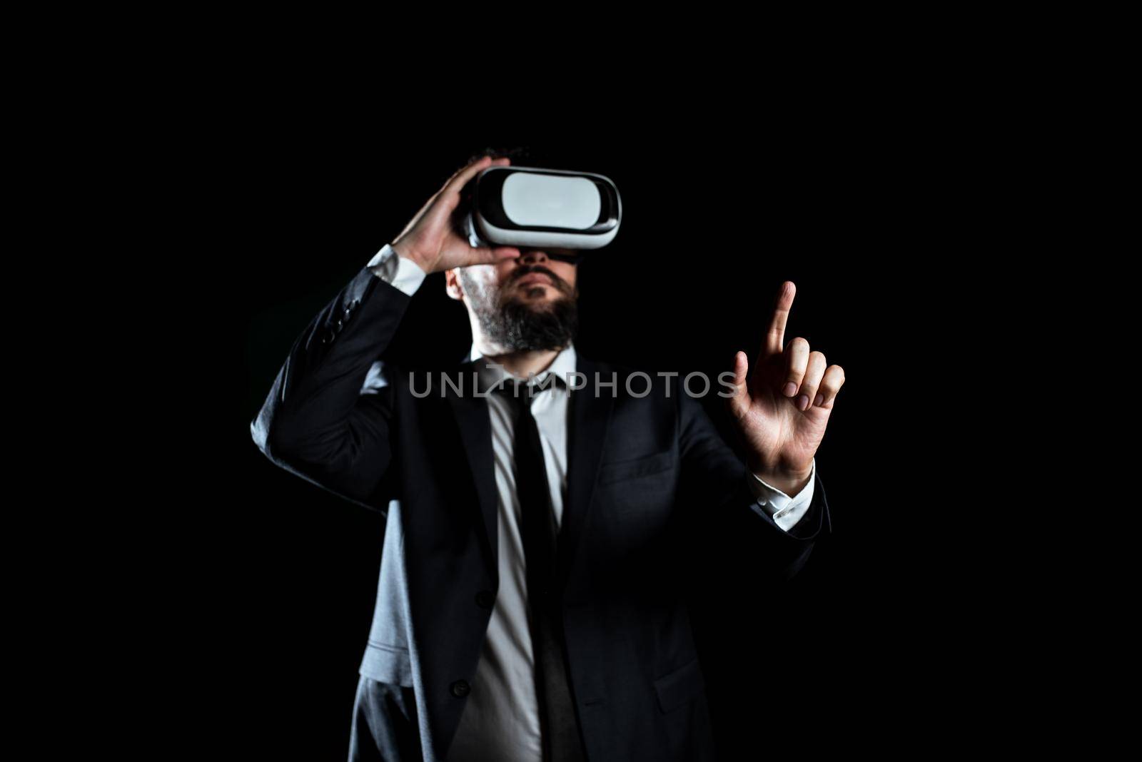 Businessman Wearing Virtual Reality Headset Gesturing And Taking Professional Training Through Simulator. Man In Suit Presenting Modern Technology Of Innovative Learning. by nialowwa