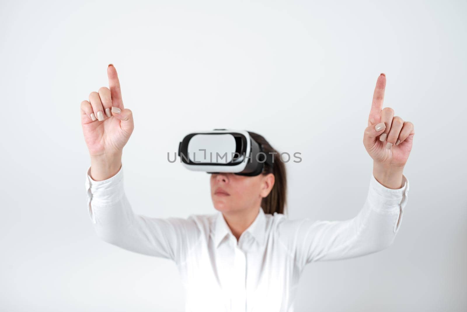 Woman Wearing Vr Glasses And Pointing On Important Messages With Both Hands. Businesswoman Having Virtual Reality Eyeglasses And Showing Crutial Informations With Two Fingers. by nialowwa