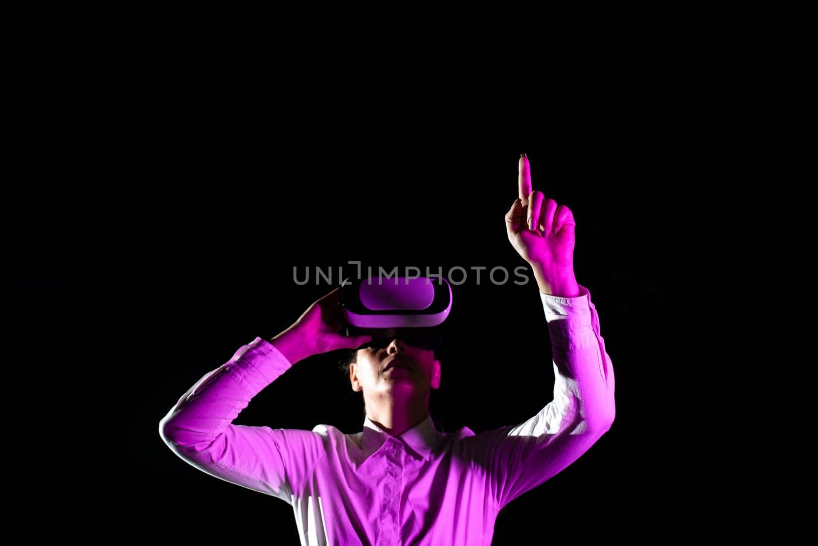 Female Manager Wearing Virtual Reality Goggles Raising Hand While Taking Professional Training. Light Falling On Woman Using Gadget And Presenting Futuristic Technology. by nialowwa