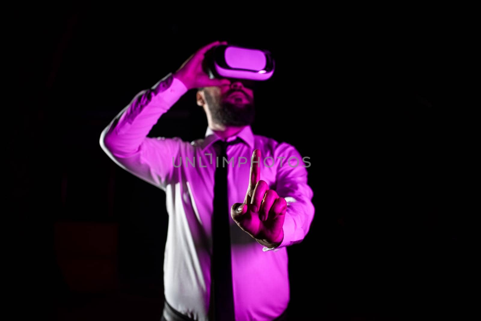 Male Professional Wearing Virtual Reality Headset Gesturing And Enjoying Simulator. Light Falling On Businessman Presenting Modern Technology And Using Futuristic Gadget. by nialowwa