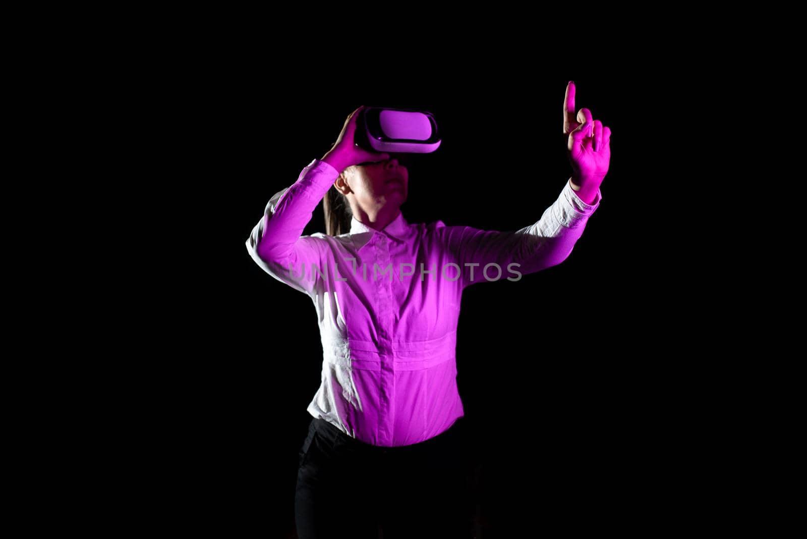 Businesswoman Using Virtual Reality Goggles Gesturing While Taking Professional Training. Light Falling On Woman Wearing Modern Simulator And Presenting Creative Technology by nialowwa