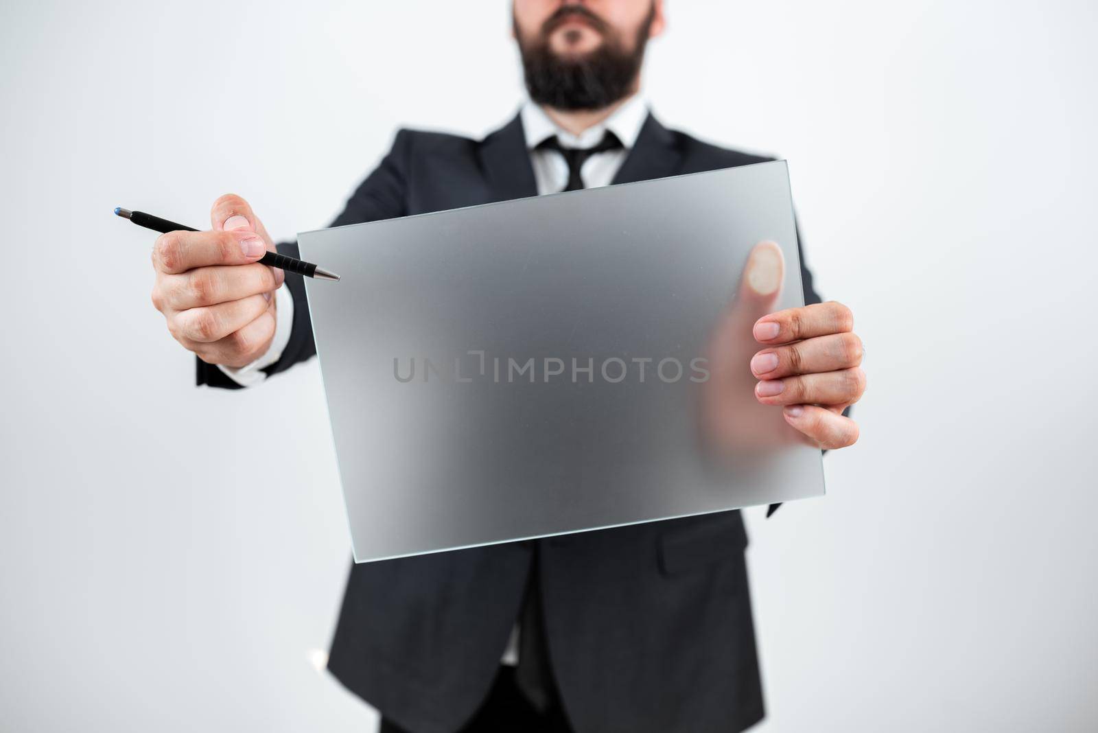 Male Professional Holding Blank Placard And Pen And Displaying Business Data. Businessman Wearing Suit Showing Rectangular Board For Marketing And Branding Of Company. by nialowwa