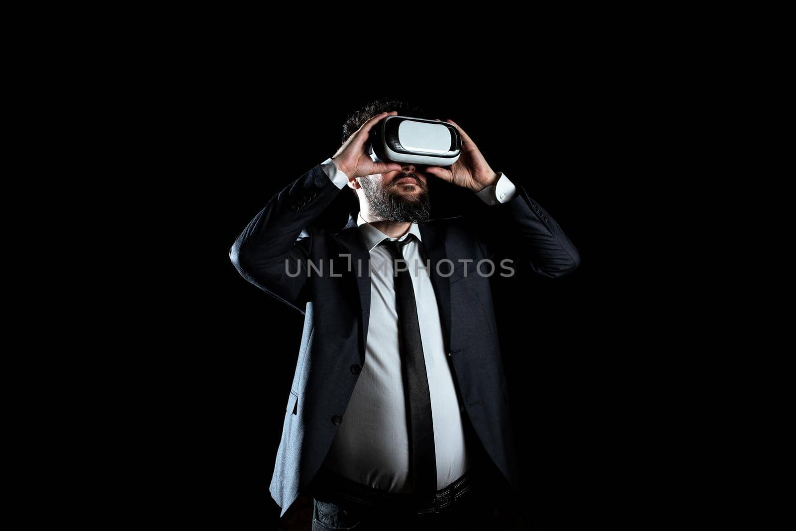 Businessman Wearing Virtual Reality Headset And Taking Professional Training Through Simulator. Man In Suit Presenting Modern Technology Of Innovative Learning. by nialowwa