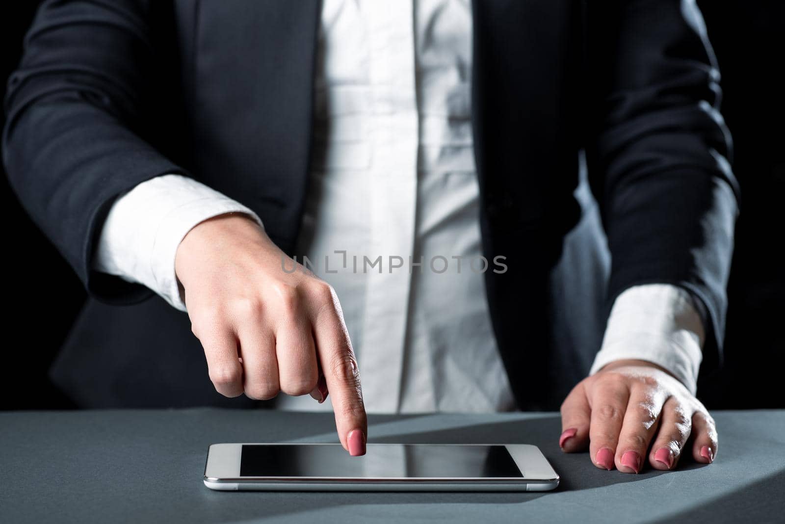 Businesswoman Having Tablet On Desk And Pointing On It With One Finger. Woman With Phone Showing Recent Updates. Executive Displaying Important News. by nialowwa