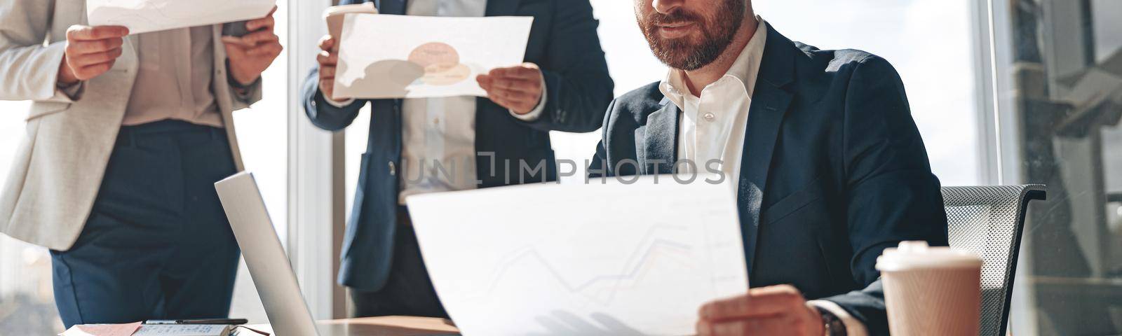 Focused businessmen discussing documents with graphs and charts in a modern office by Yaroslav_astakhov
