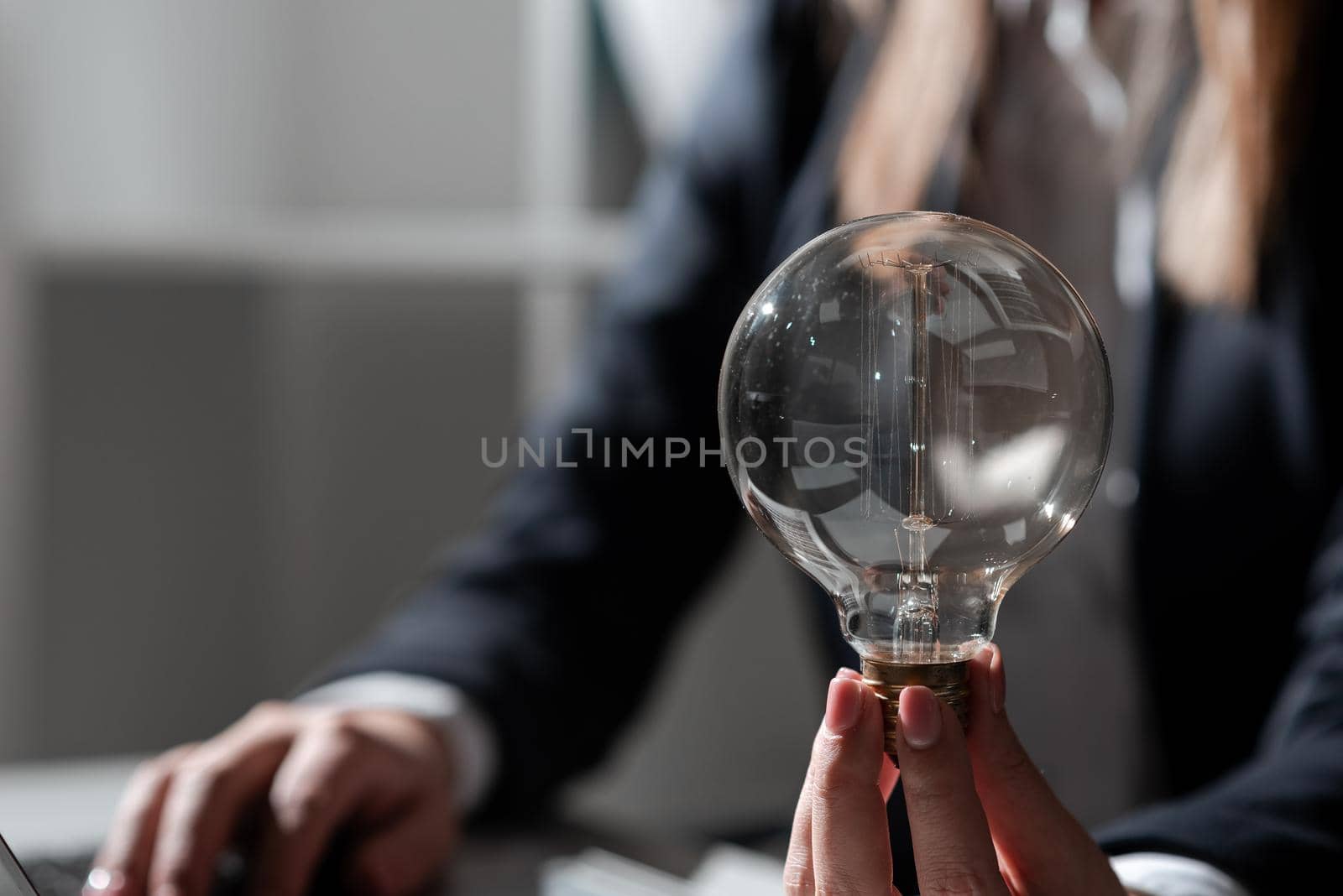 Businesswoman Typing Recent Updates On Lap Top On Desk Holding Lightbulb.