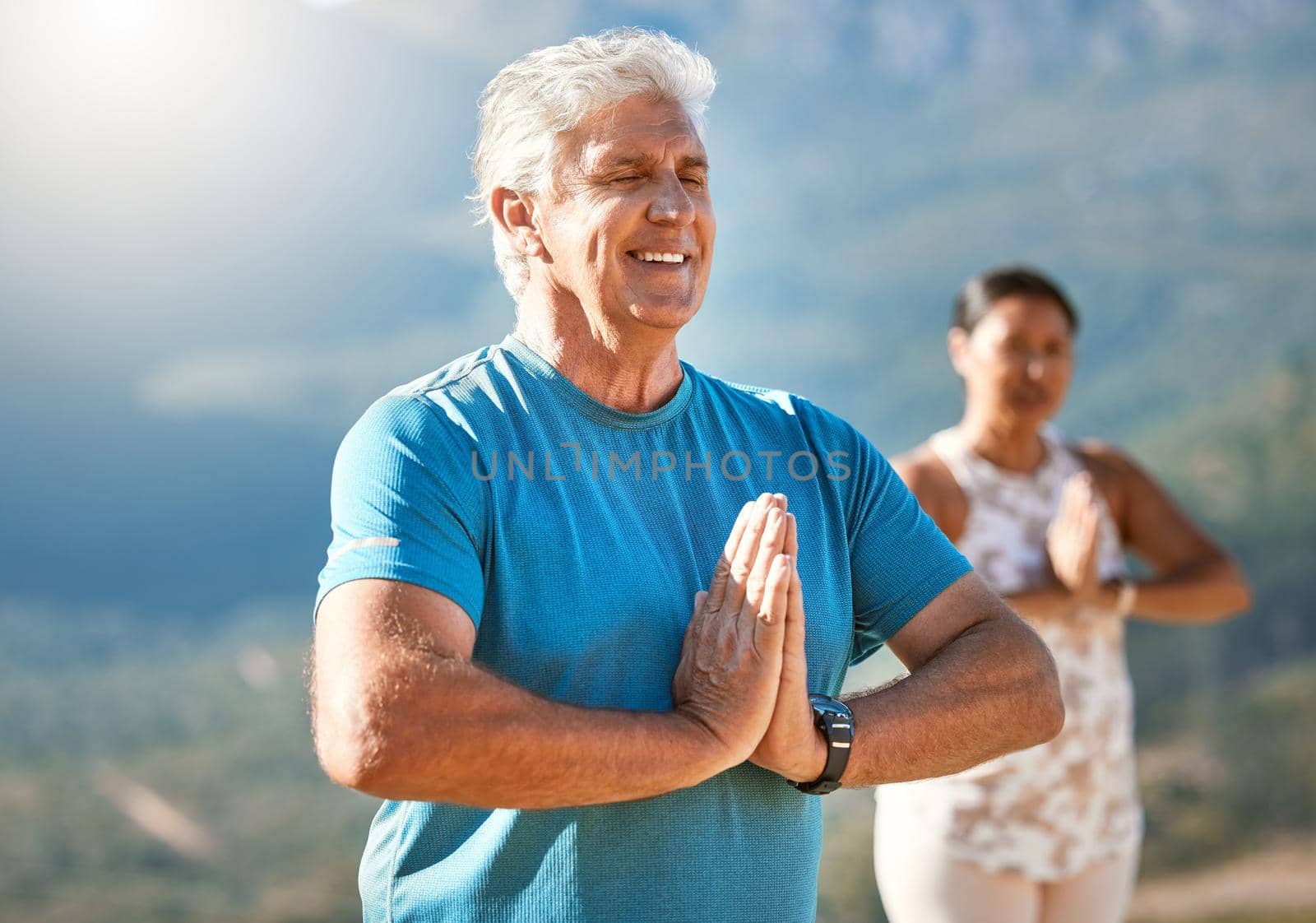 Senior man meditating with joined hands and closed eyes breathing deeply. Mature people doing yoga in nature living a healthy active lifestyle in retirement by YuriArcurs