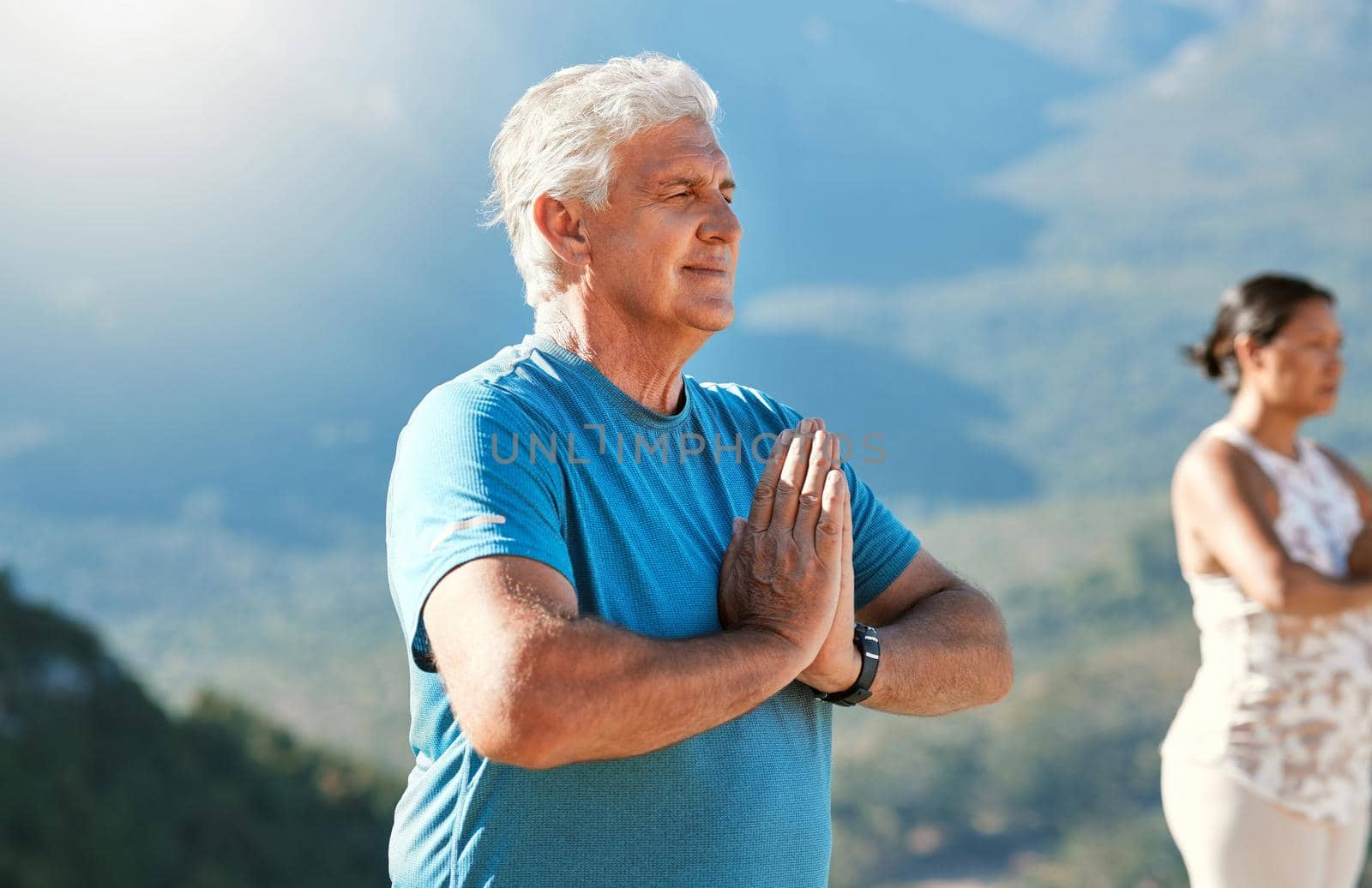 Senior man meditating with joined hands and closed eyes breathing deeply. Mature people doing yoga in nature living a healthy active lifestyle in retirement.