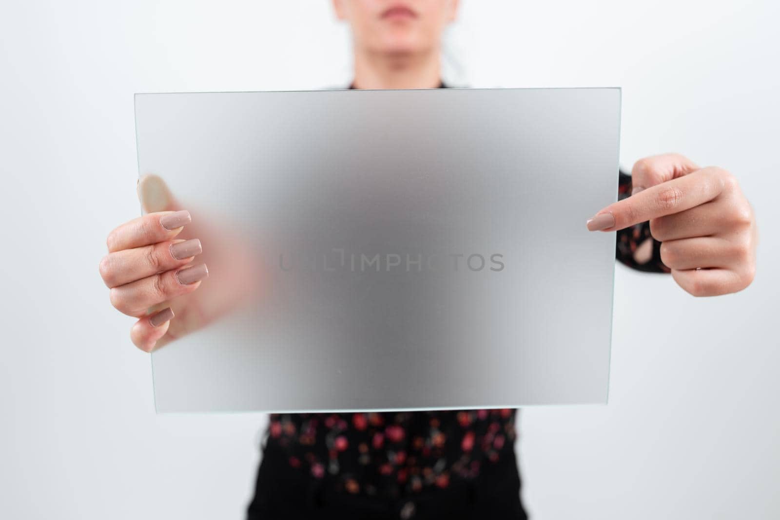 Businesswoman Holding And Pointing At Blank Placard While Making Crucial Announcement. Woman Showing Board With New Ideas And Strategies For Business Marketing. by nialowwa