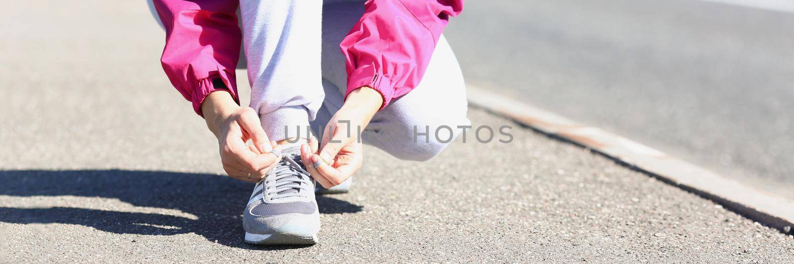 Low angle of woman runner tying laces before training on fresh air in park. Going to tun marathon in sportswear. Sport, physical activity, hobby concept