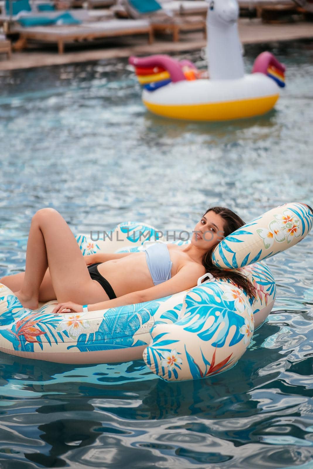 Woman on inflatable Flamingo floating in swimming pool. Girl relaxing sunbathing enjoying travel holidays