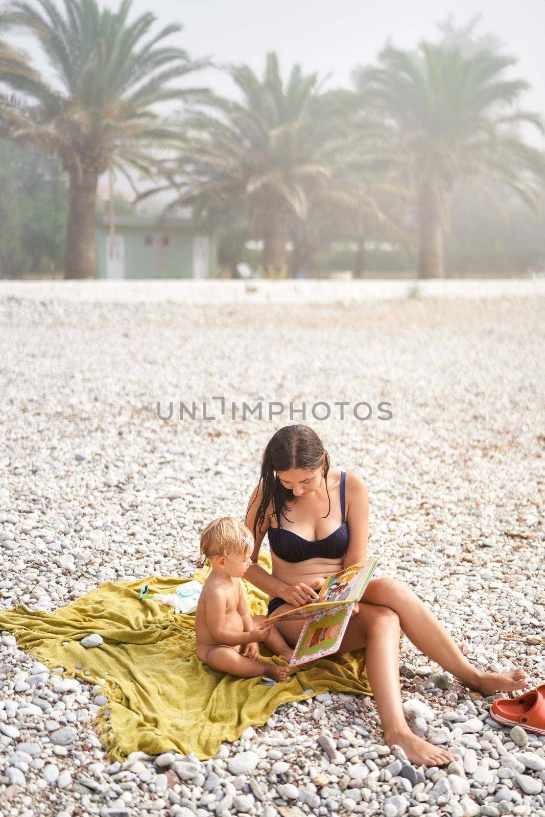 Mom reads a book to a little girl sitting on the beach. High quality photo