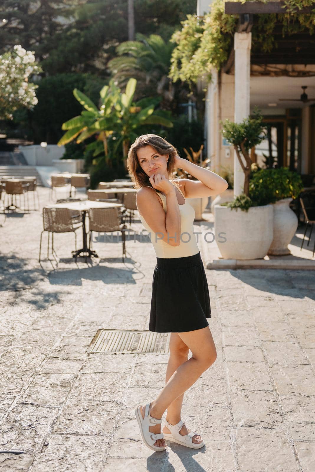 Girl Tourist Walking Through Ancient Narrow Street On A Beautiful Summer Day In MEDITERRANEAN MEDIEVAL CITY, OLD TOWN BUDVA, MONTENEGRO. Young Beautiful Cheerful Woman Walking On Old Street At Tropical Town. Pretty Girl Looking At You And Smiling by Andrii_Ko