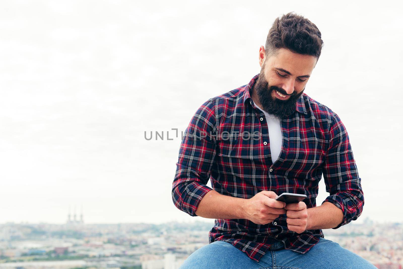 portrait of a handsome bearded man typing a text message on his mobile phone, concept of freedom and technology , copy space for text