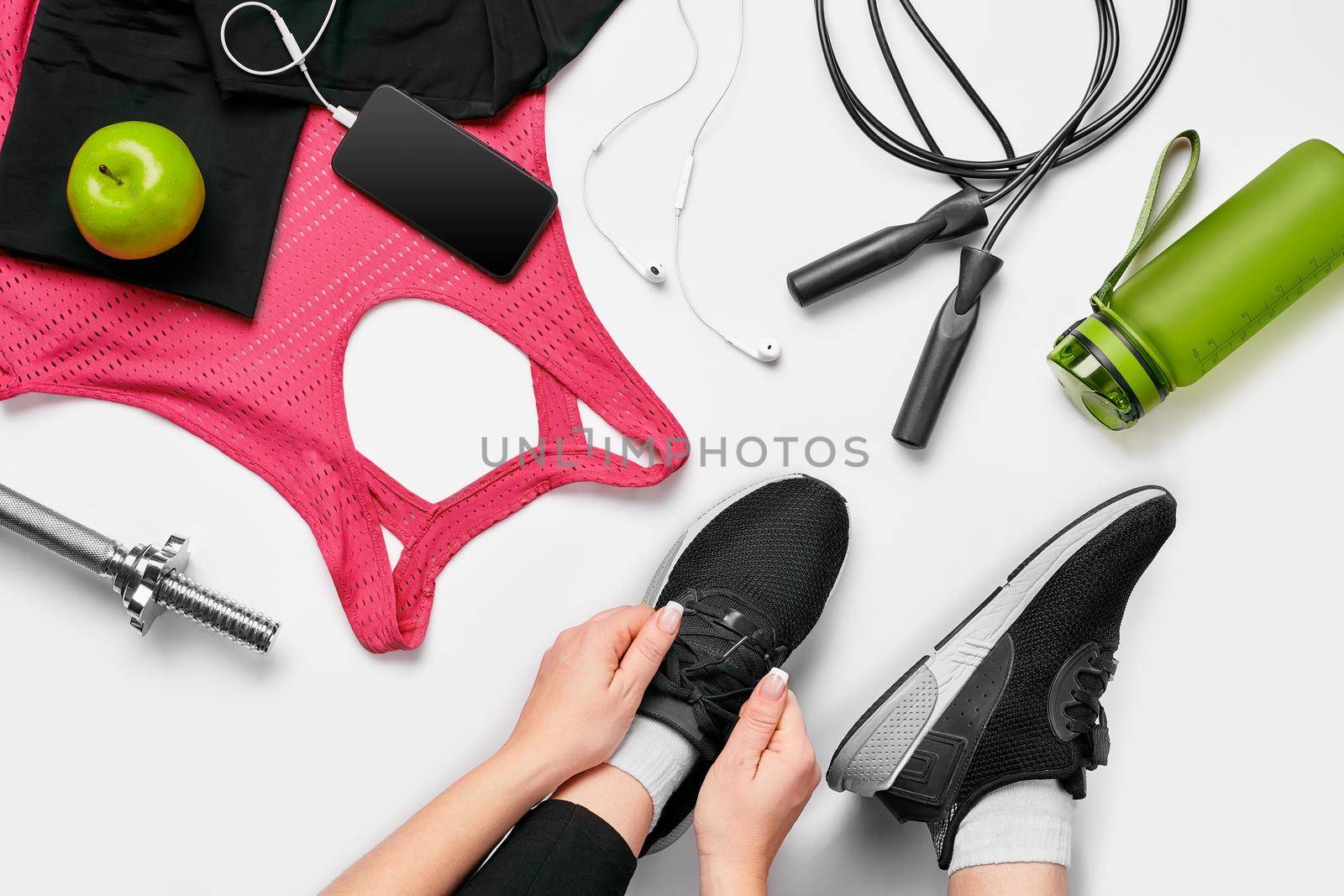 Overhead view of woman hands tying shoes with sport equipments on white background. Top view. Still life. Sports shoes, Fitness concept