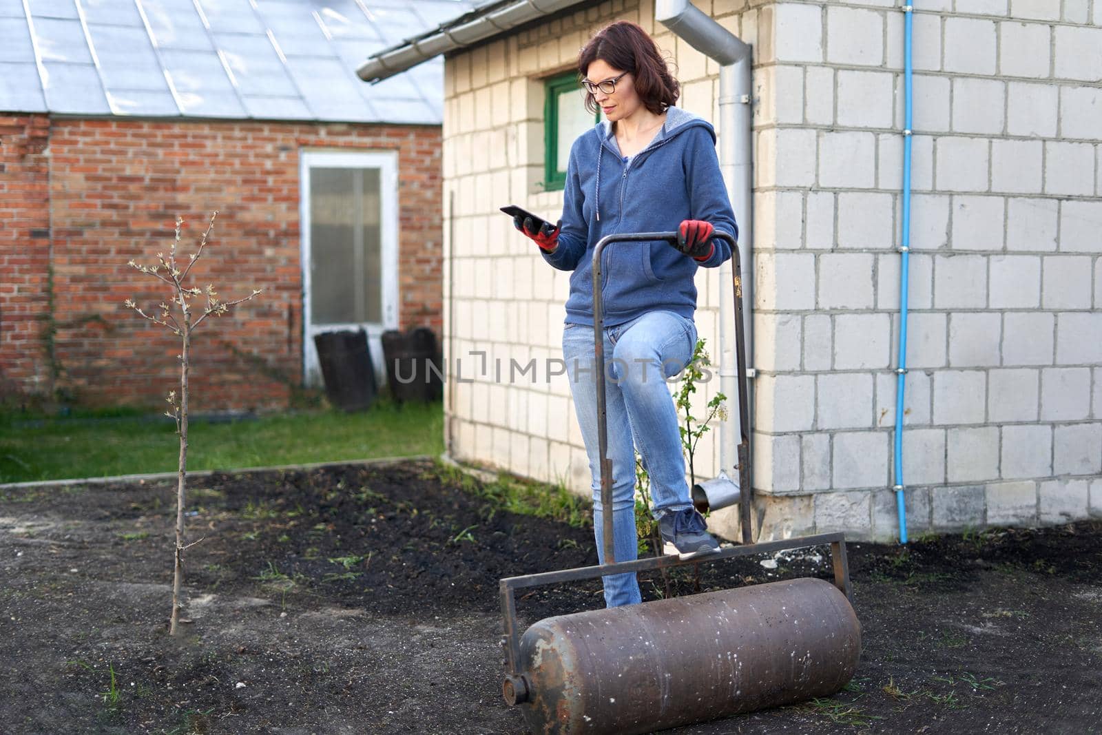 Woman using the mobile while flattening the land for a home vegetable garden by WesternExoticStockers