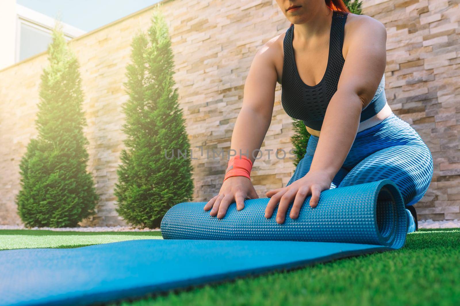 cropped shot of a young sportswoman, unrolling a mat for yoga exercises. unrecognisable girl doing sports exercises at home. concept of health and wellness. by CatPhotography