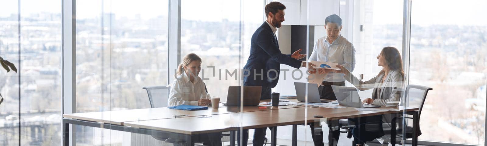 People standing near table, team of young businessmen working and communicating together in office.