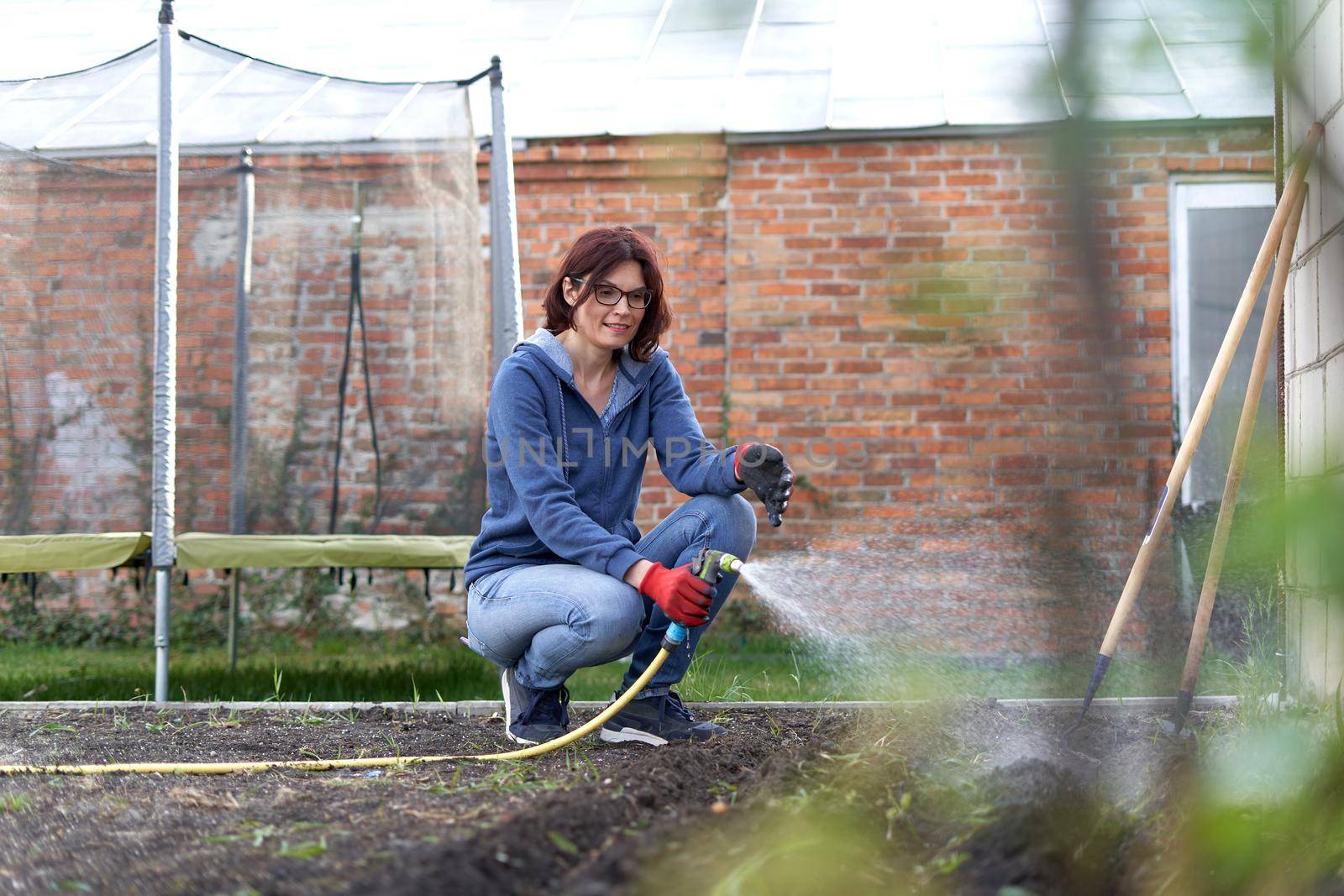 Happy woman watering plants in the garden of a house by WesternExoticStockers