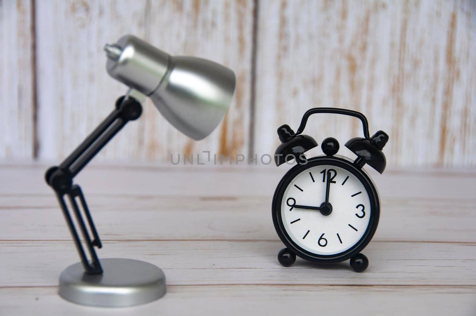 Alarm clock pointing at 9 o'clock with table lamp on wooden background. Copy space and time concept