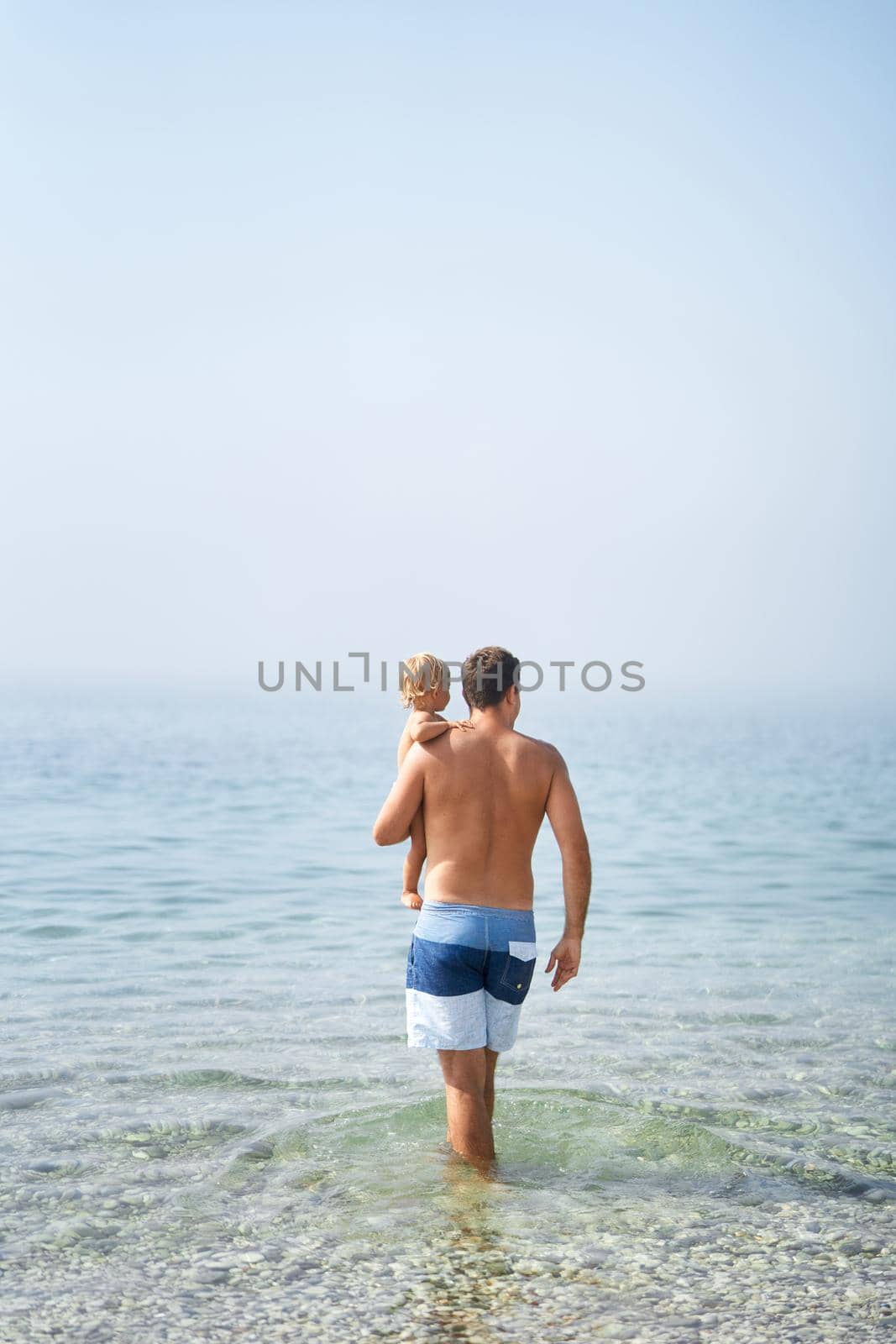 Dad with a little girl in his arms walks through the shallow sea. High quality photo